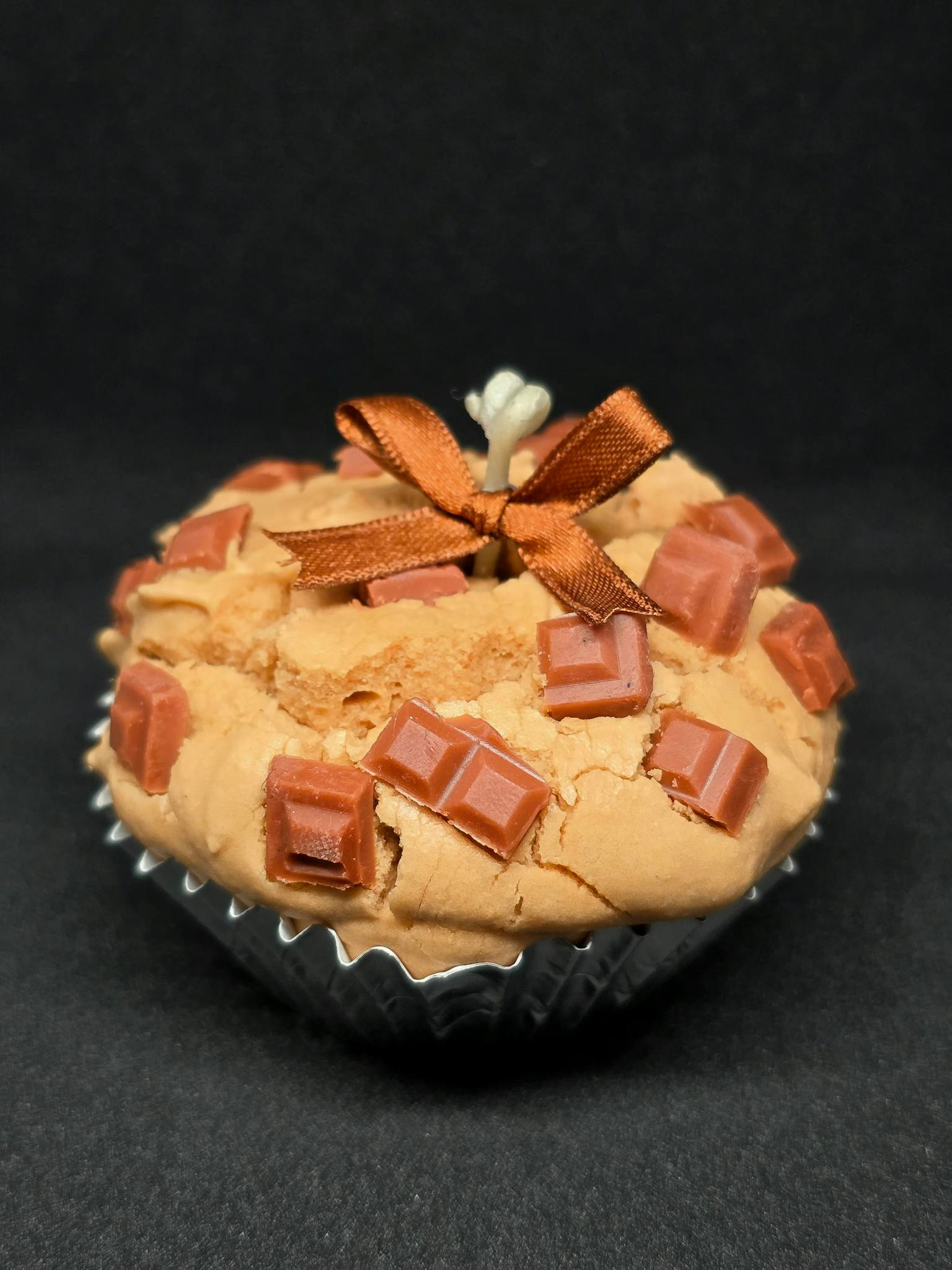 A close-up of a cupcake topped with chocolate chunks and a decorative ribbon.