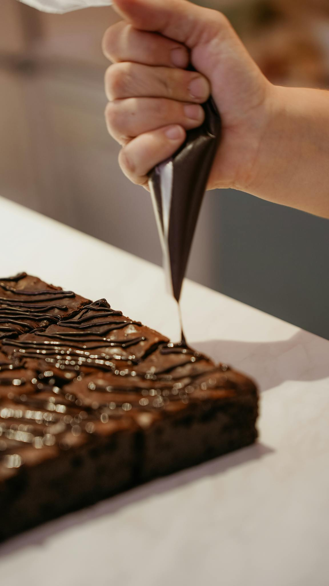 Close-up of hand icing chocolate brownies, showcasing homemade dessert preparation.